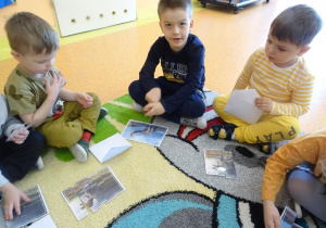 Trójka dzieci siedzi na dywanie, każde dziecko układa obrazek z części przedstawiający dinozaura.
